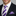Man wearing a black suit with a white shirt, purple and white striped tie, and matching pocket square.