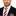 Man wearing a black suit with a red and white striped tie and checkered pocket square on a white background