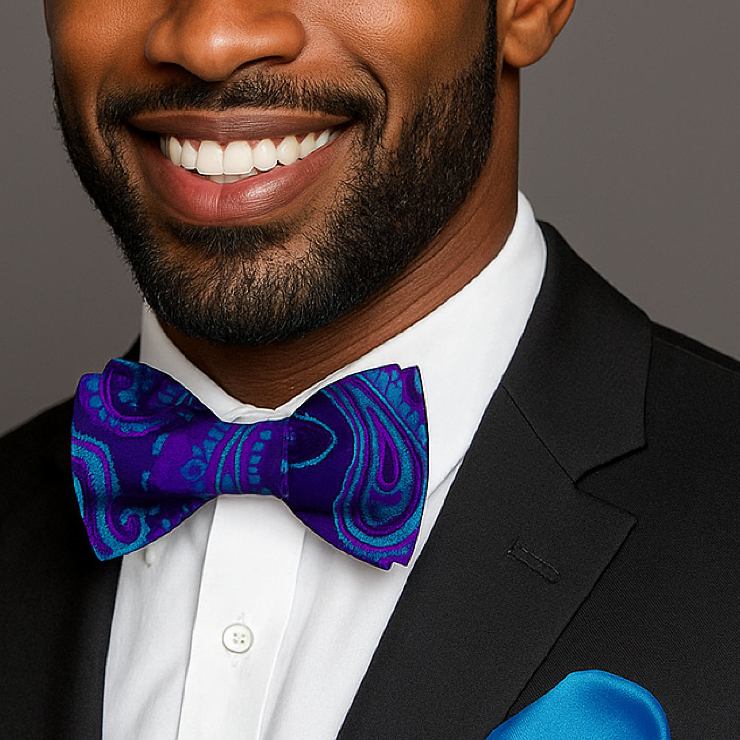 Man wearing a black suit with a white shirt and blue paisley bow tie, smiling.