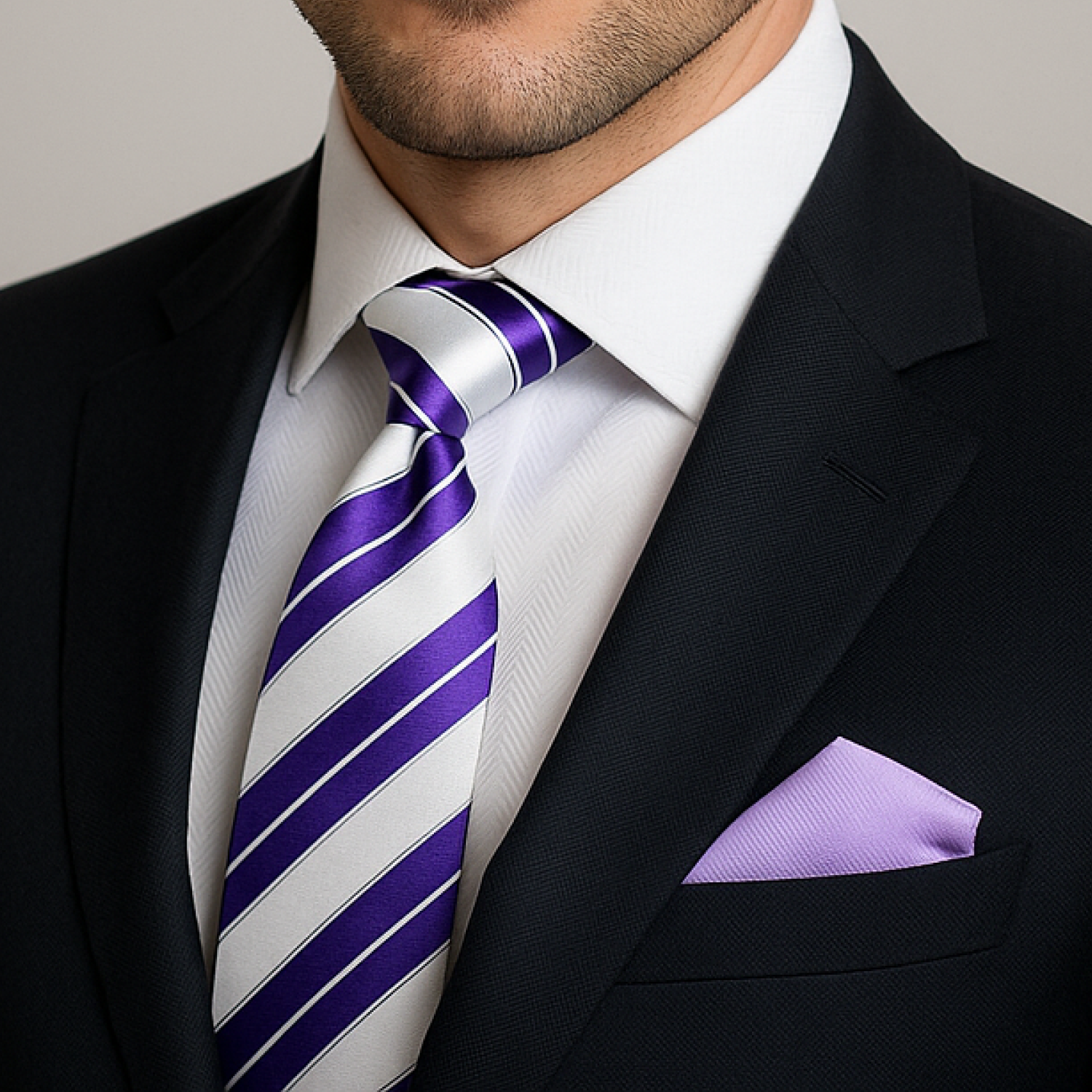 Man wearing a black suit with a white shirt, purple striped tie, and light purple pocket square.