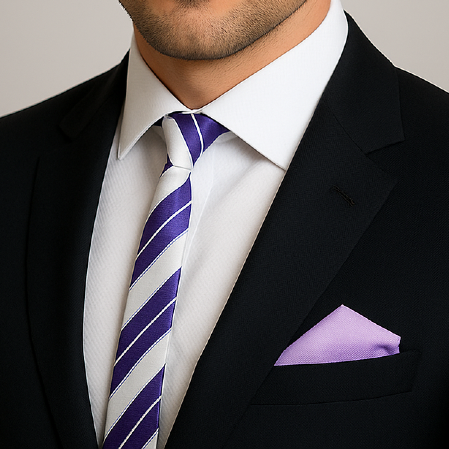 Man wearing a black suit with a white shirt, purple striped thin tie, and light purple pocket square.