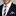 Man wearing a black suit with a white shirt, purple and white striped thin tie, and matching pocket square.