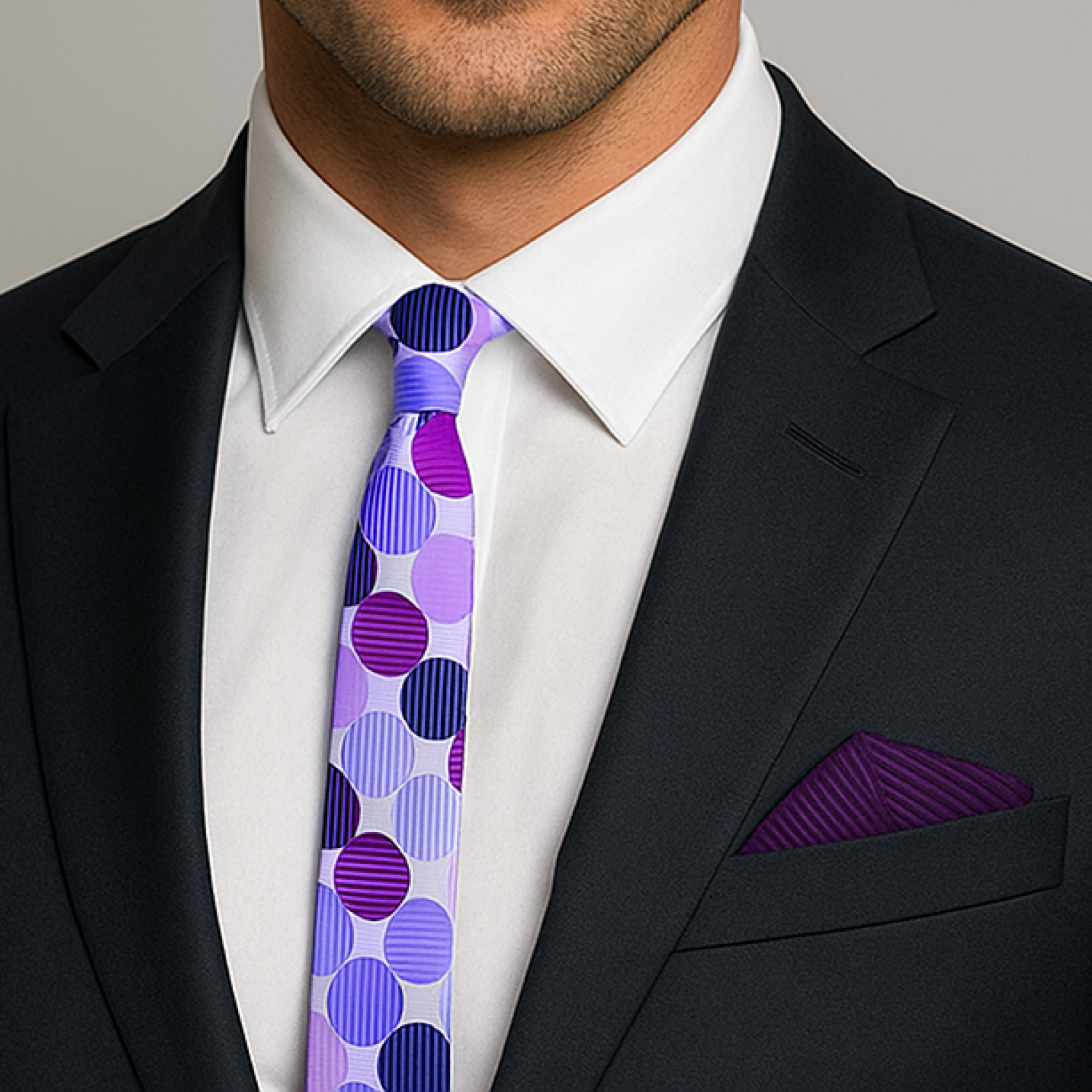 Man wearing a black suit with a white shirt and a purple polka dot tie.