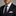 Man wearing a black suit with a pink pocket square and dark tie against a neutral background