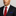 Man wearing a black suit with a red tie and blue pocket square against a gray background