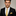 Man wearing a black suit with a yellow tie and pocket square against a neutral background