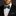 Man wearing a black tuxedo with a green polka dot bow tie against a dark background