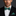 Man wearing a black suit with a green polka dot bow tie and pocket square against a dark background
