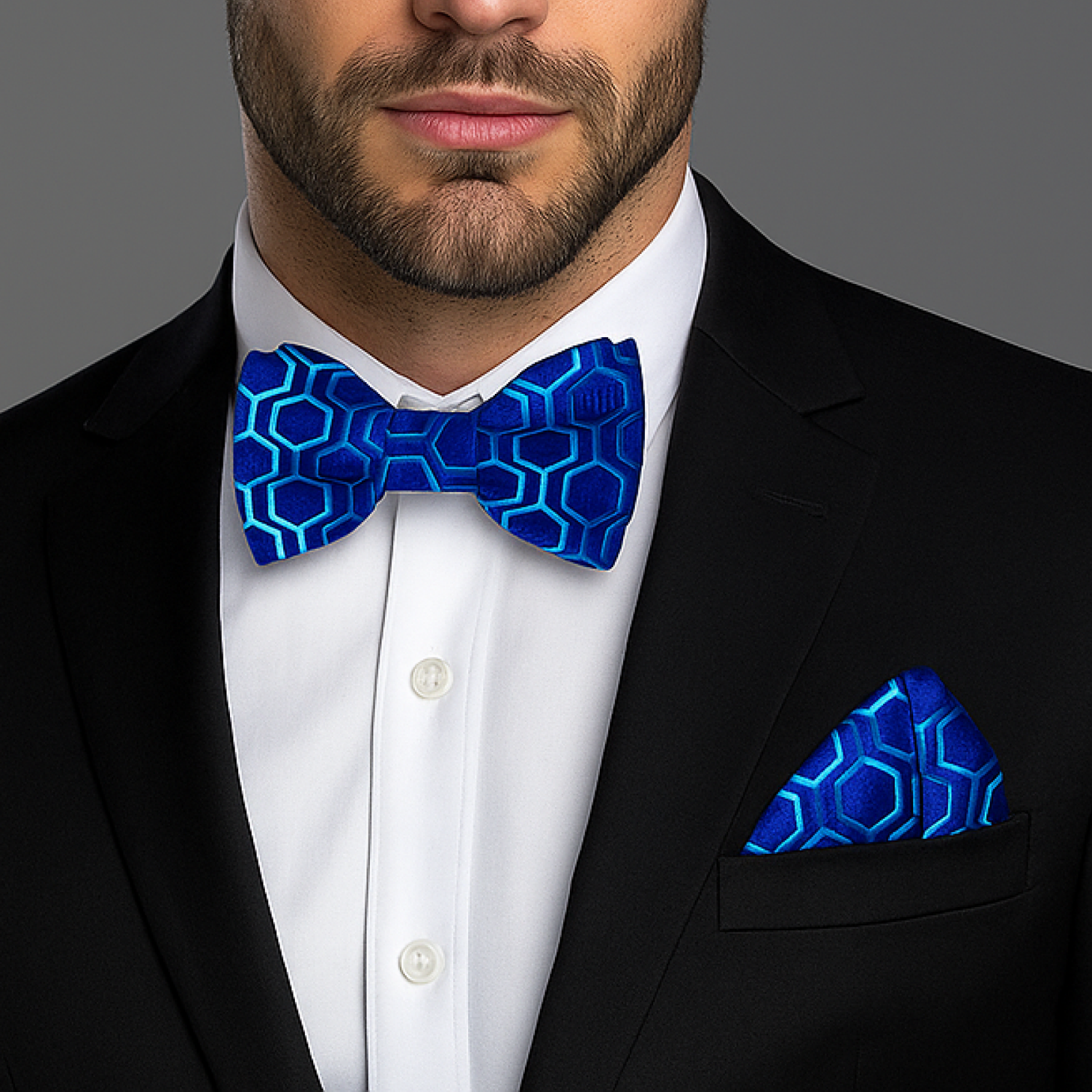 Man wearing a black suit with a blue geometric bow tie and pocket square against a gray background