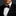 Man wearing a black tuxedo with a red geometric patterned bow tie and pocket square on a dark background.