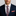 Man wearing a navy suit with a plaid tie and coral pocket square on a gray background