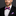 Man wearing a black suit with a pink and blue striped bow tie and pocket square against a dark background