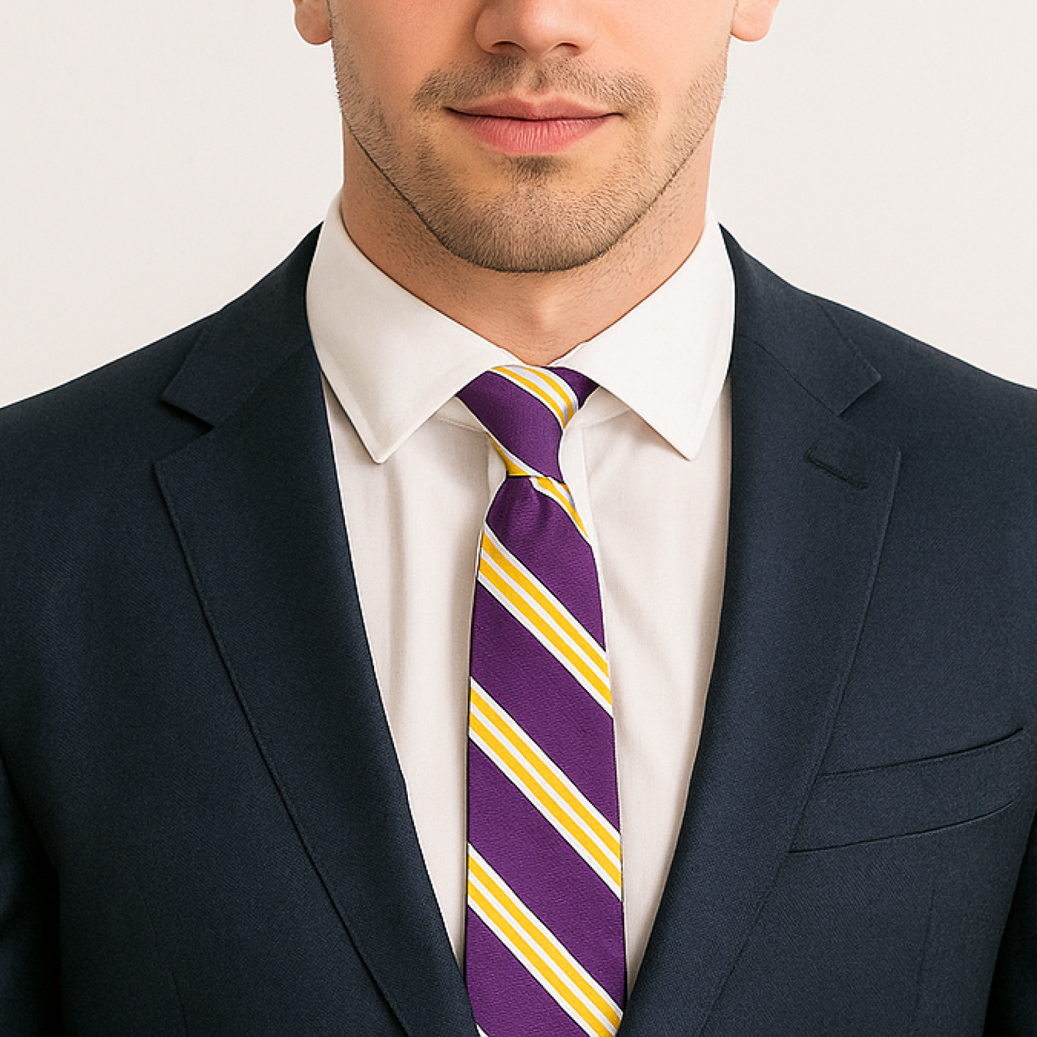 Man wearing a navy suit with a white shirt and purple striped tie on a plain background