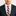Man wearing a navy suit with a white shirt and purple striped tie on a plain background