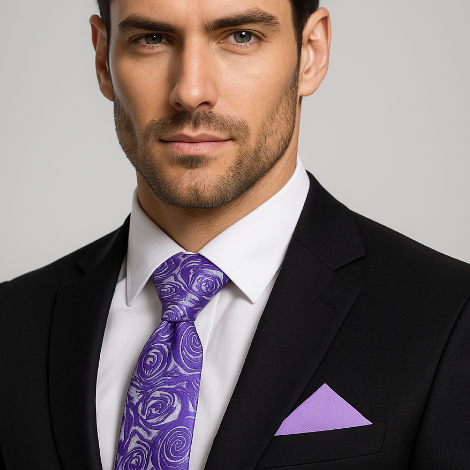 Man wearing a black suit with a purple tie and pocket square against a gray background
