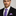 Man wearing a black suit with a purple tie and pocket square against a gray background