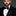 Man wearing a black suit with a white shirt and purple bow tie and pocket square on a gray background