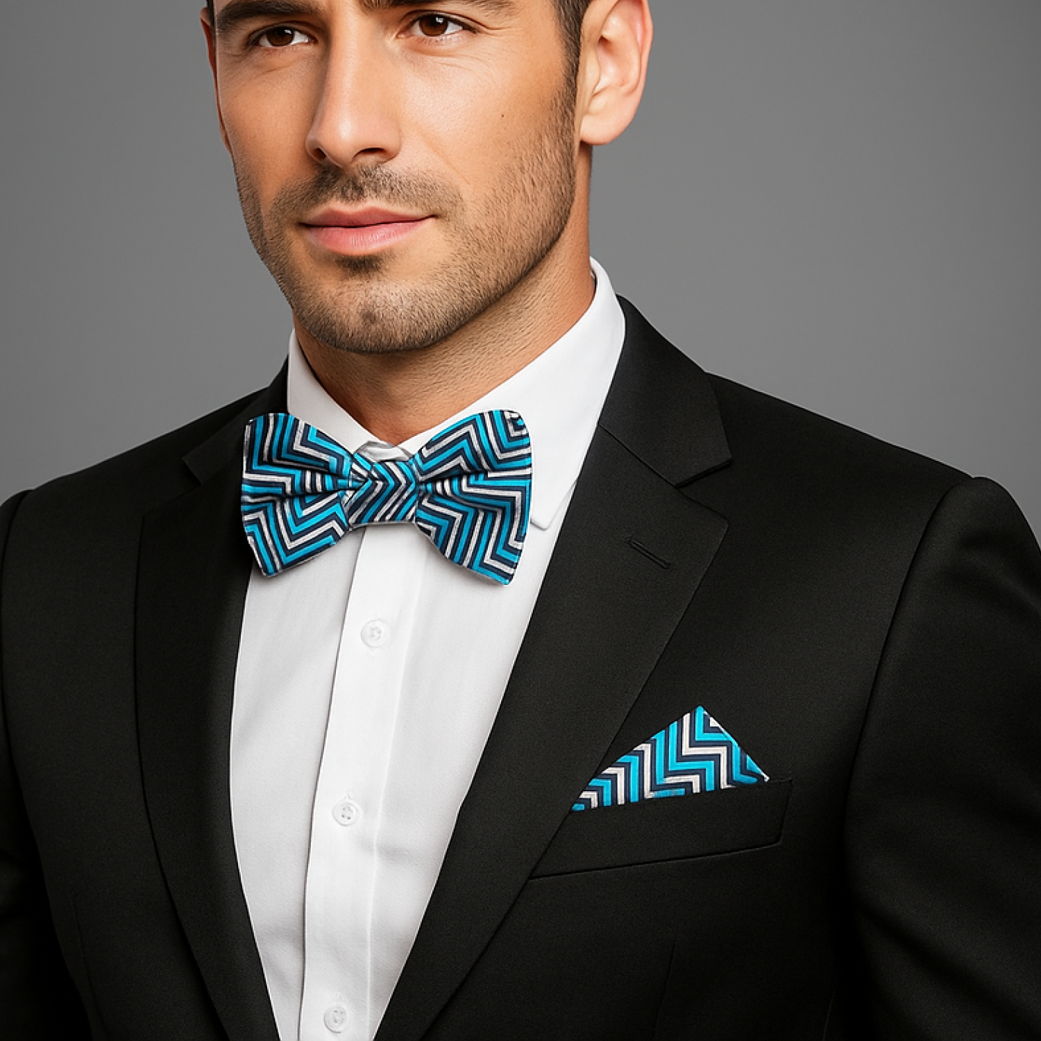 Man wearing a black suit with a blue geometric bow tie and pocket square on a gray background