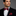 Man wearing a black suit with a red and blue striped bow tie and pocket square on a gray background