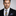 Man wearing a suit with a striped tie and patterned pocket square on a gray background