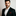 Man wearing a black suit with a red pocket square on a plain background
