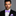 Man wearing a black suit with a purple bow tie and pocket square on a gray background