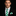 Man wearing a black suit with a green and white striped tie and pocket square on a black background