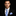 Man wearing a black suit with a blue striped tie and pocket square on a dark background