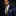 Man wearing a navy suit with a yellow and blue striped tie against a dark background