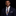Man wearing a navy suit with a plaid tie and pocket square on a black background