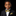 A young boy wearing a black suit jacket, white dress shirt, black bow tie, and a matching gold pocket square against a solid black background.