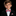 A young boy with brown hair wearing a black suit jacket, white dress shirt, and a red and white geometric patterned bow tie and pocket square, set against a solid black background.