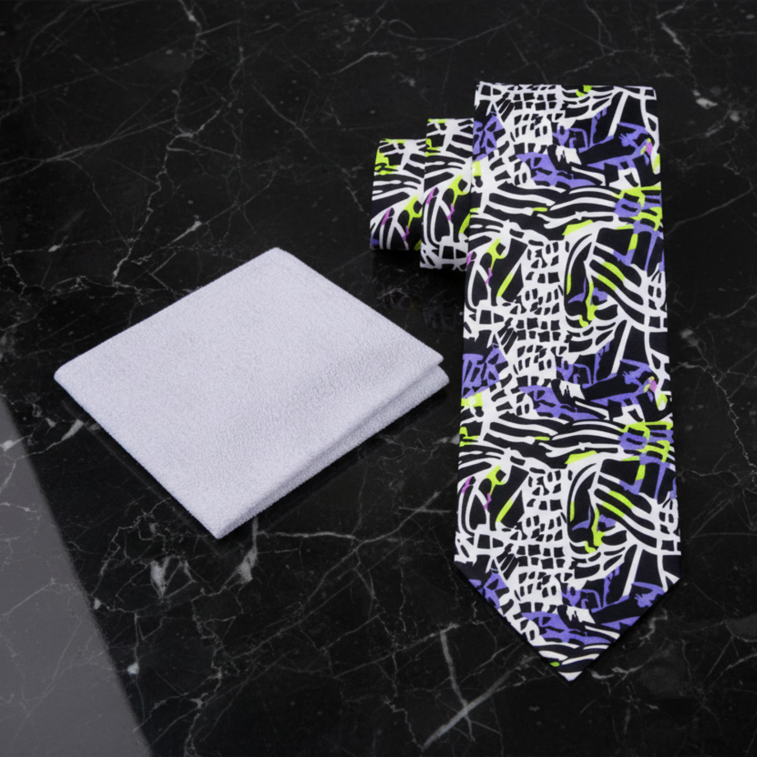 Colorful tie with abstract pattern next to a light gray square on a marble background