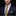 Man wearing a navy suit with a yellow patterned tie and pocket square on a black background