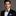 Man wearing a black suit with a patterned bow tie and blue handkerchief on a gray background