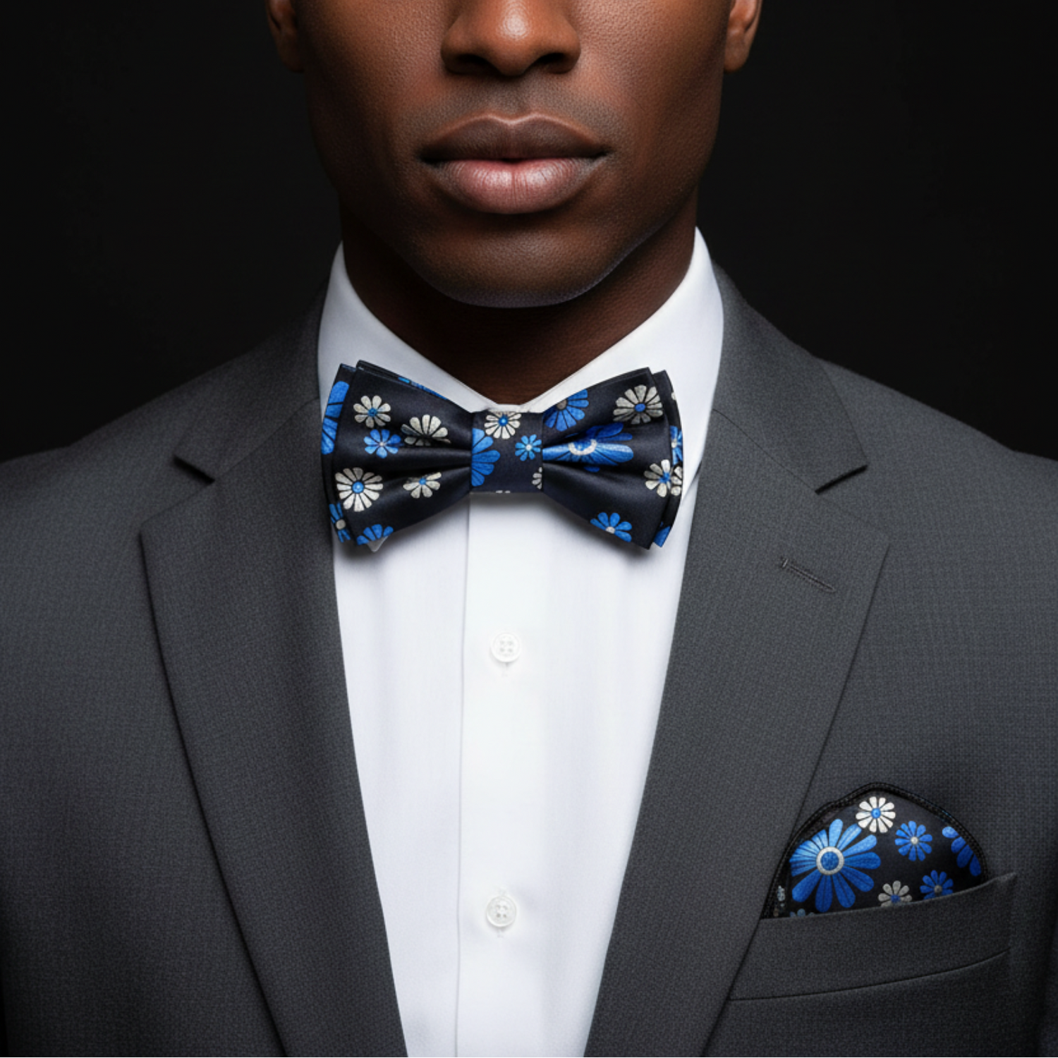 Man wearing a gray suit with a blue floral bow tie and pocket square against a black background