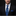 Man wearing a black suit with a blue paisley tie and pocket square on a black background