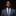 Man wearing a gray suit with a blue patterned tie and pocket square on a black background