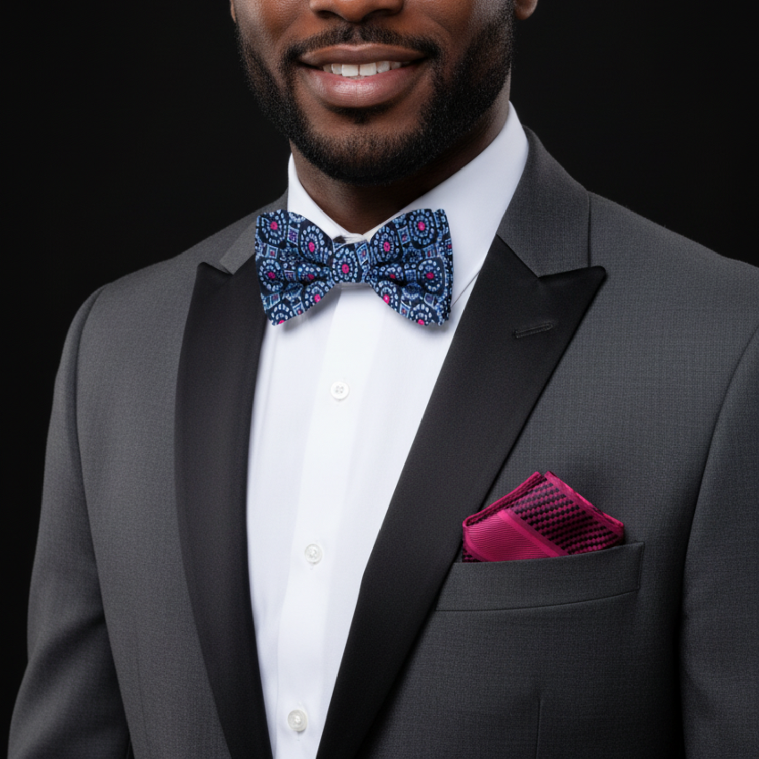 Man wearing a gray tuxedo with a colorful bow tie and pink handkerchief on a black background