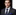 Man wearing a dark suit with a blue tie and pocket square on a black background