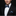 Man wearing a black suit with a blue and black striped bow tie and pocket square on a black background