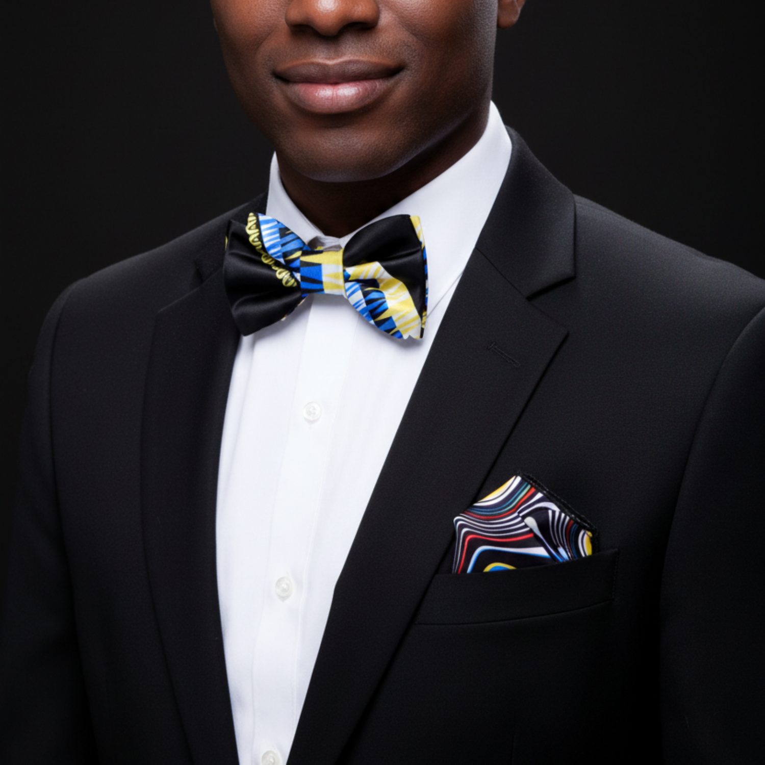 Man wearing a black suit with a colorful bow tie and pocket square against a dark background