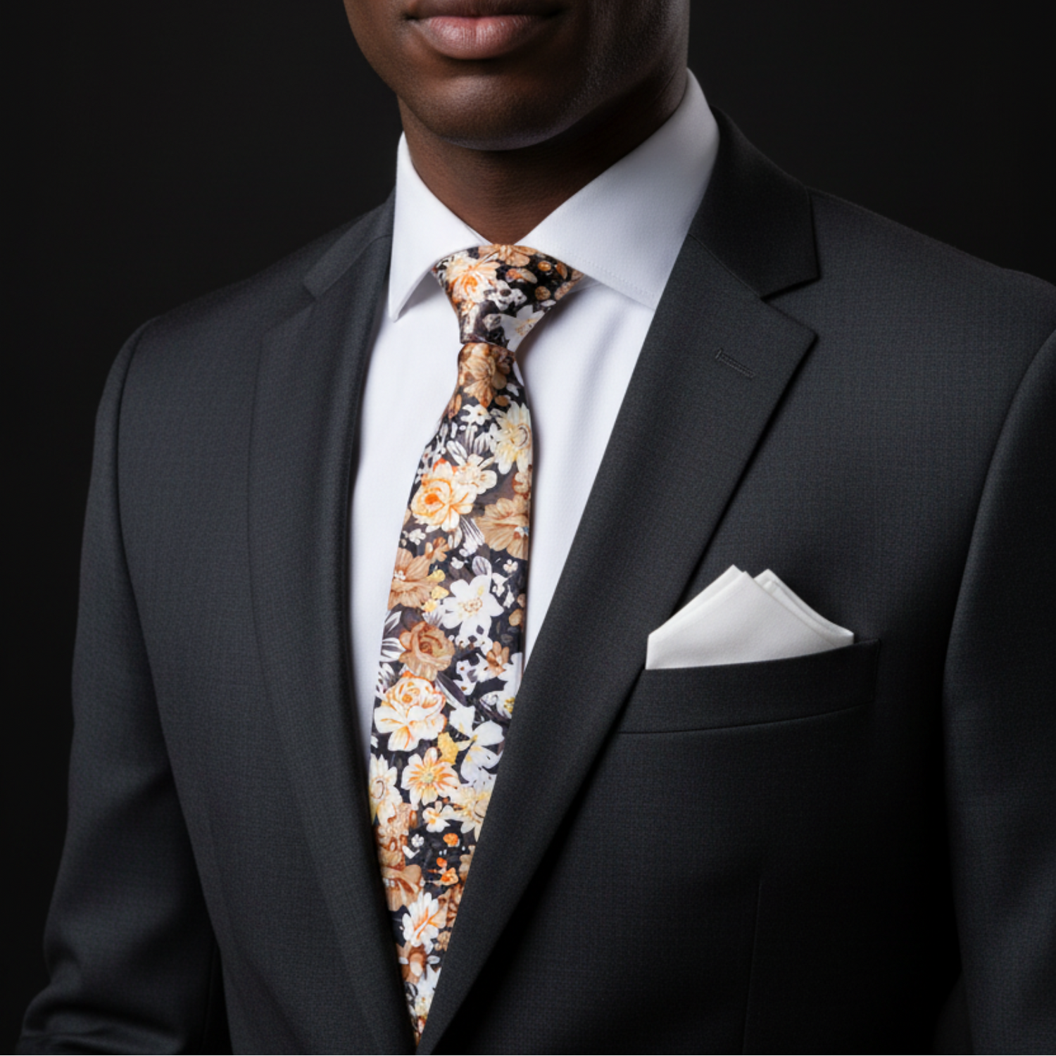 Man wearing a black suit with a floral tie and white pocket square on a dark background