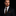 Man wearing a dark suit with a striped tie and pocket square on a black background