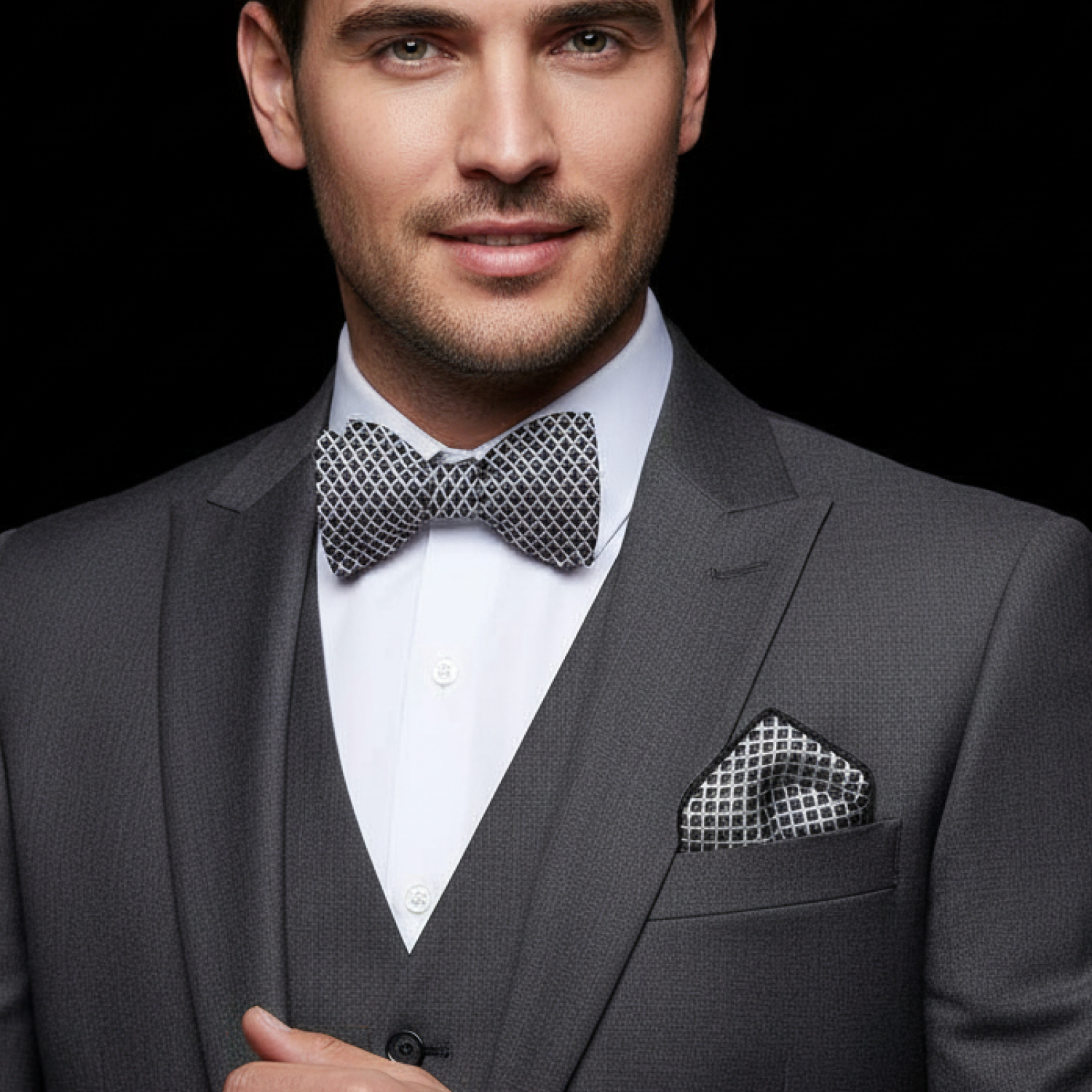 Man wearing a gray suit with a patterned bow tie and pocket square on a black background