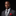 Man wearing a gray suit with a striped tie and red pocket square on a black background