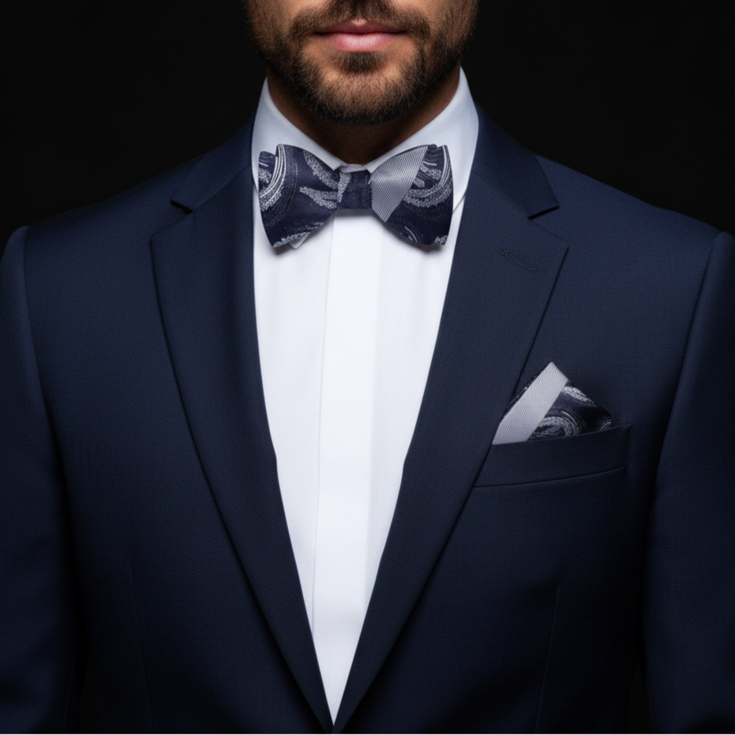 Man wearing a navy suit with a patterned bow tie and pocket square on a black background