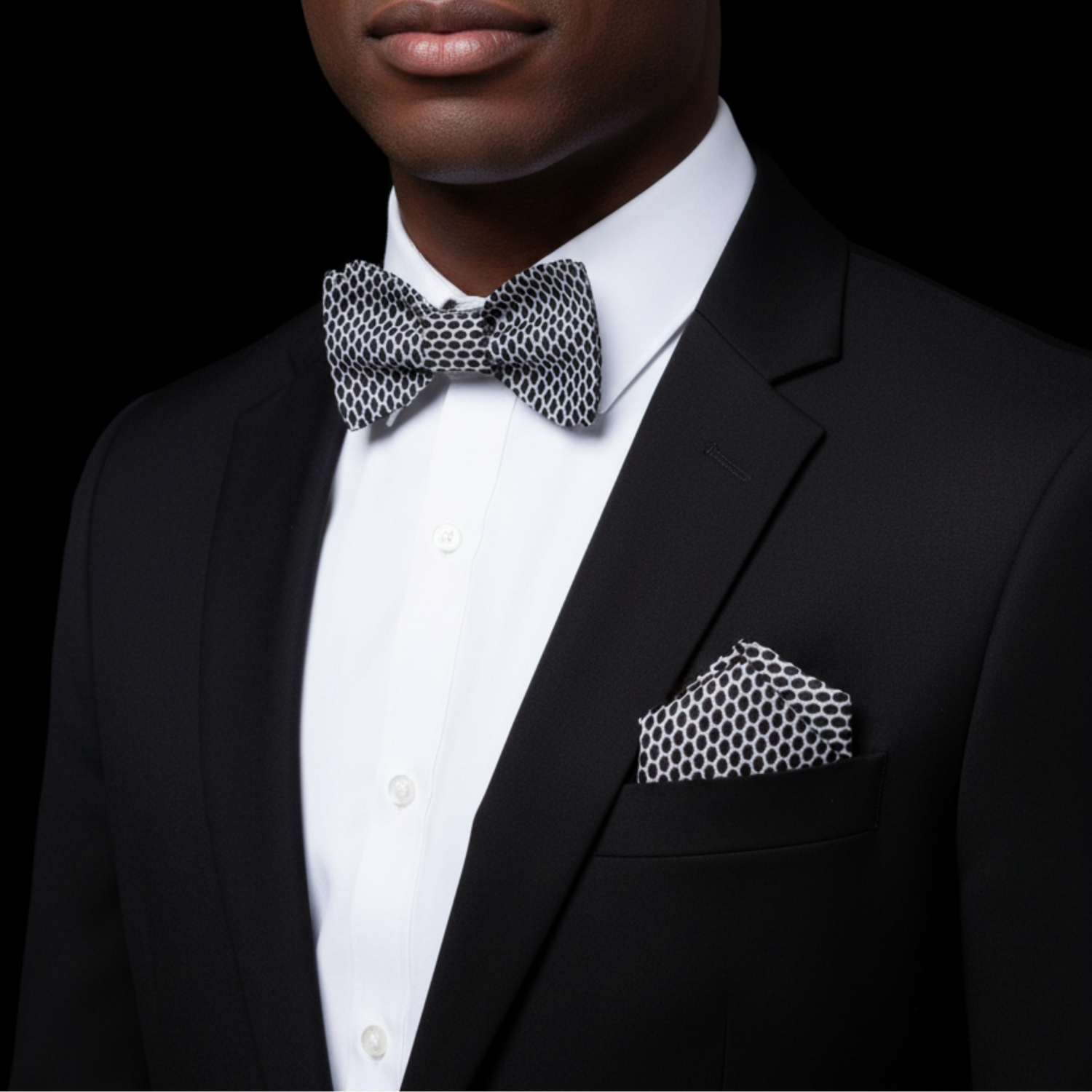 Man wearing a black suit with a patterned bow tie and pocket square on a black background
