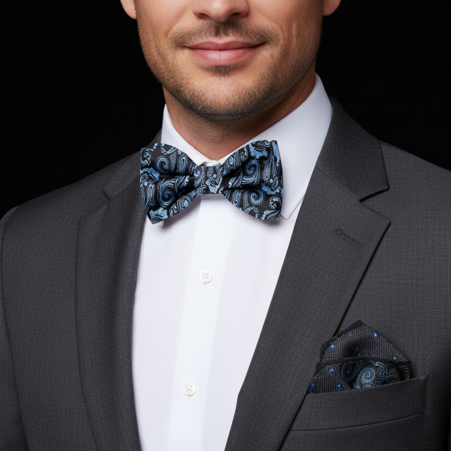 Man wearing a gray suit with a white shirt and blue paisley bow tie on a black background