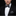 Man wearing a black tuxedo with a white shirt, black bow tie with white polka dots, and patterned pocket square on a black background.